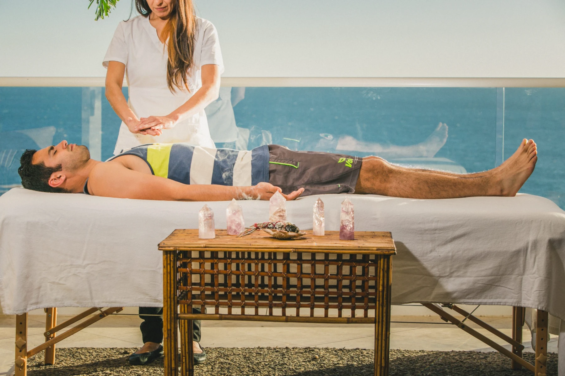 Energy Healing Session on the Oceanfront Terrace A practitioner delivering an energy healing session to a guest on a treatment table on the oceanfront terrace at Holistic Sanctuary, with healing crystals arranged on a table alongside